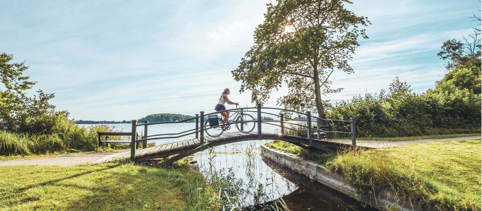Woman cycling on a scenic wooden bridge in Denmark. | Daniel Villadsen