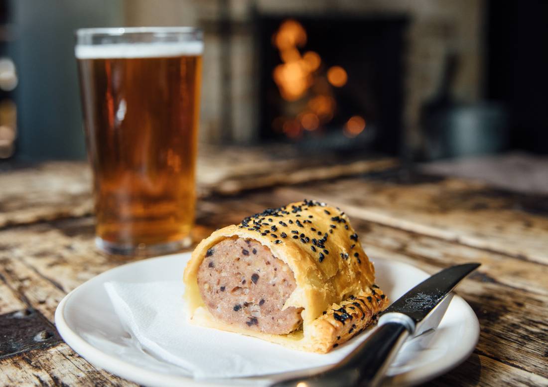 A delicious pint of beer and hot sausage roll in a pub in England.
