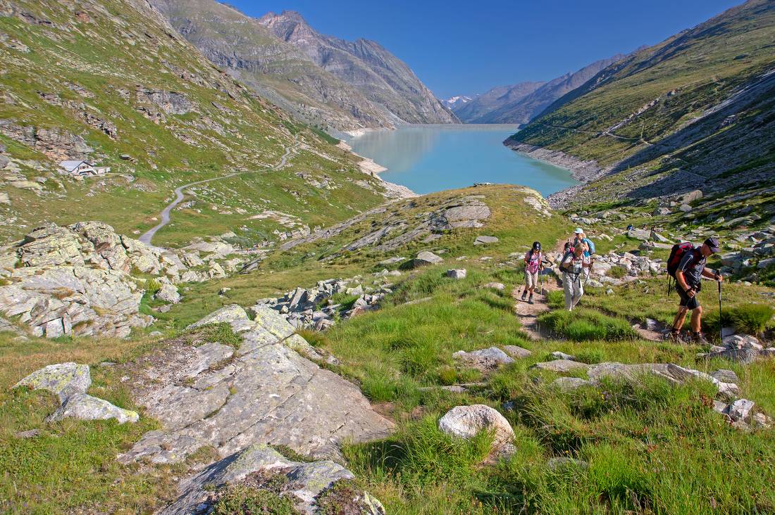 Group ascending a mountain on the Tour de Monte Rosa Walk above a stunning alpine lake |  <i>Andrew Bain</i>