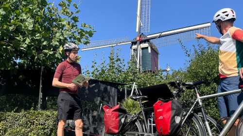 Cycling the Pieterpad Trail, two riders pause beside a windmill in the Netherlands.