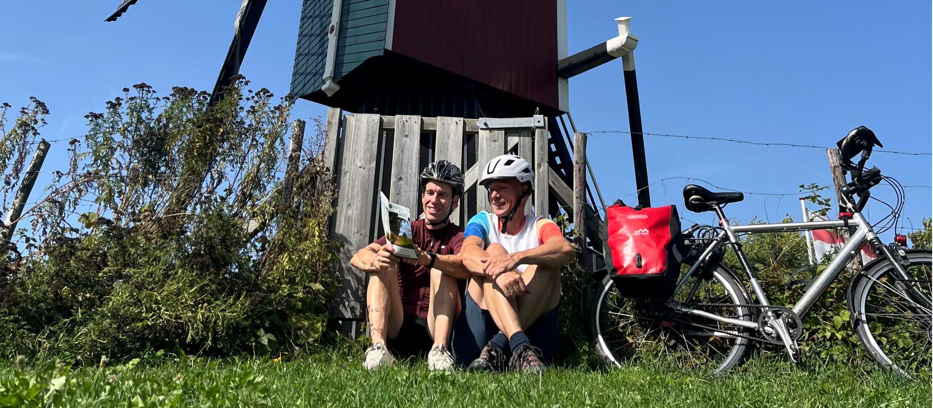 Pieterpad Trail cyclists rest beside a traditional windmill, Netherlands.