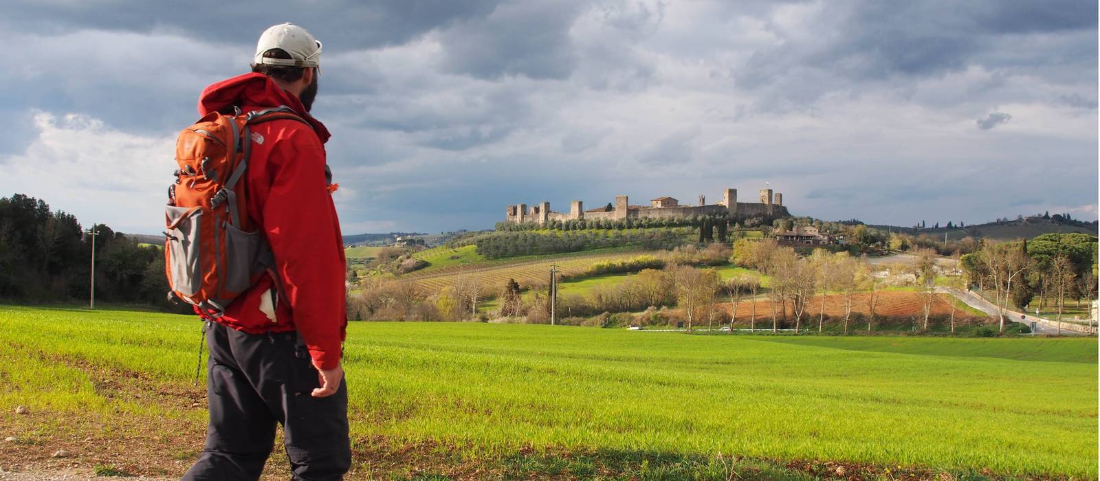 A walker admiring the hilltop town of Monteriggioni on the Via Francigena, Italy | Brad Atwal