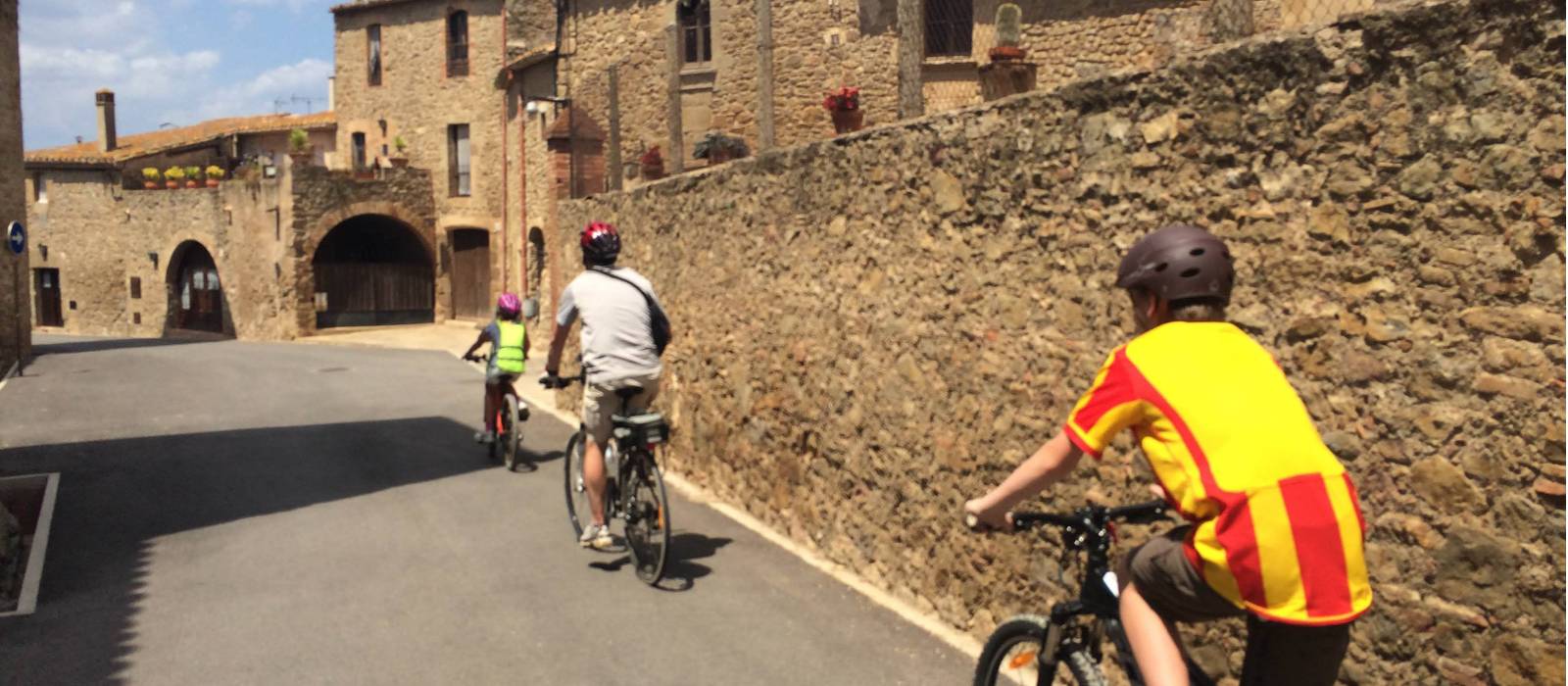 Family cycling through a village in Catalonia on a self guided cycle trip | Kate Baker