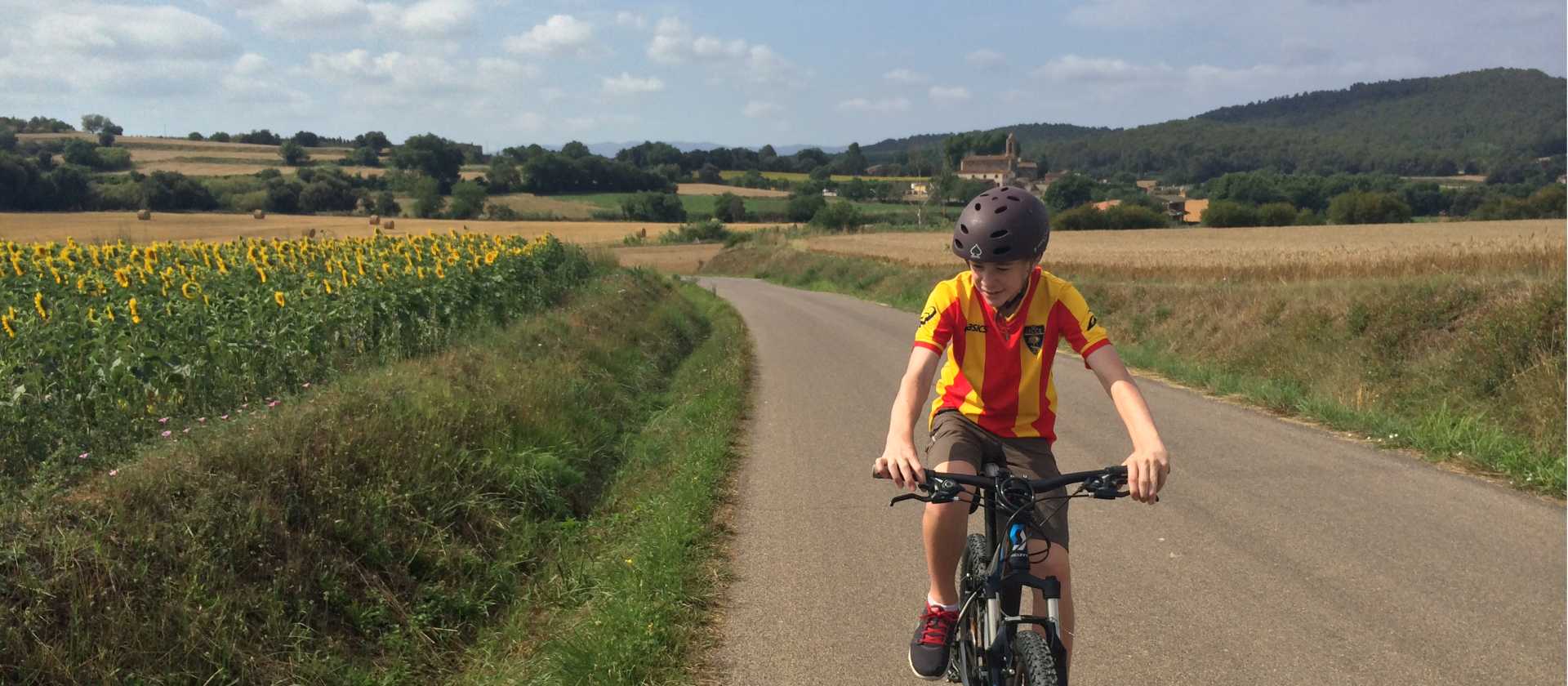 teenage boy cycling past sunflowers on a self guided cycle trip in Catalonia | Kate Baker