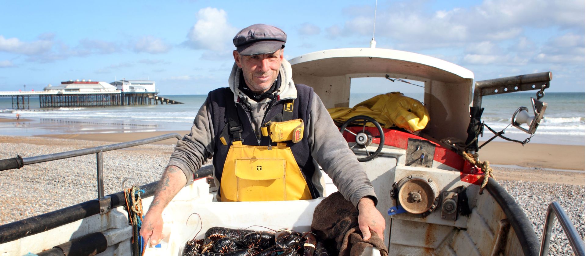 Norfolk Coast Path fisherman sorting crab catch beside his boat on Cromer beach
