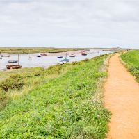 Norfolk Coast Path leads past moored boats on the salt marsh