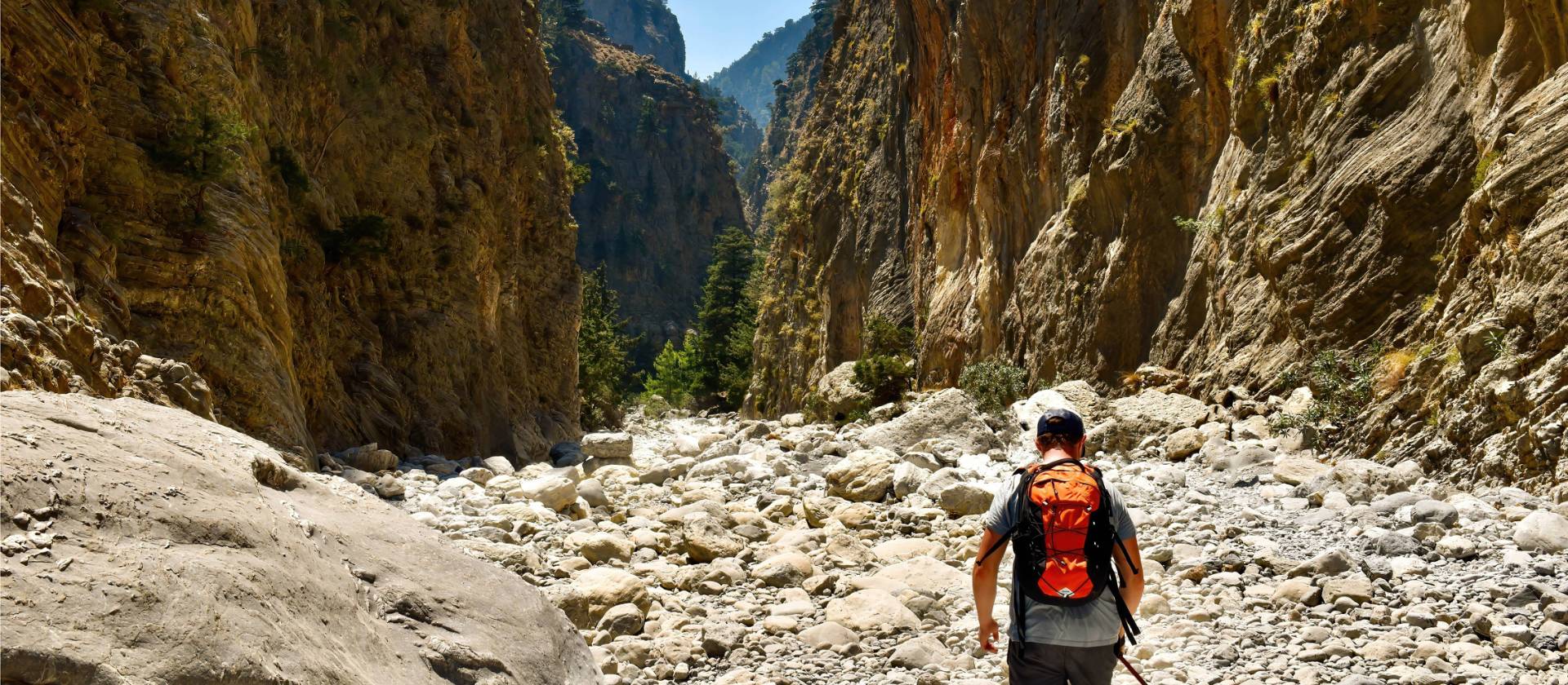 Man with orange backpack hiking in mountain valleys by hot summertime in Samaria Gorge in Greece