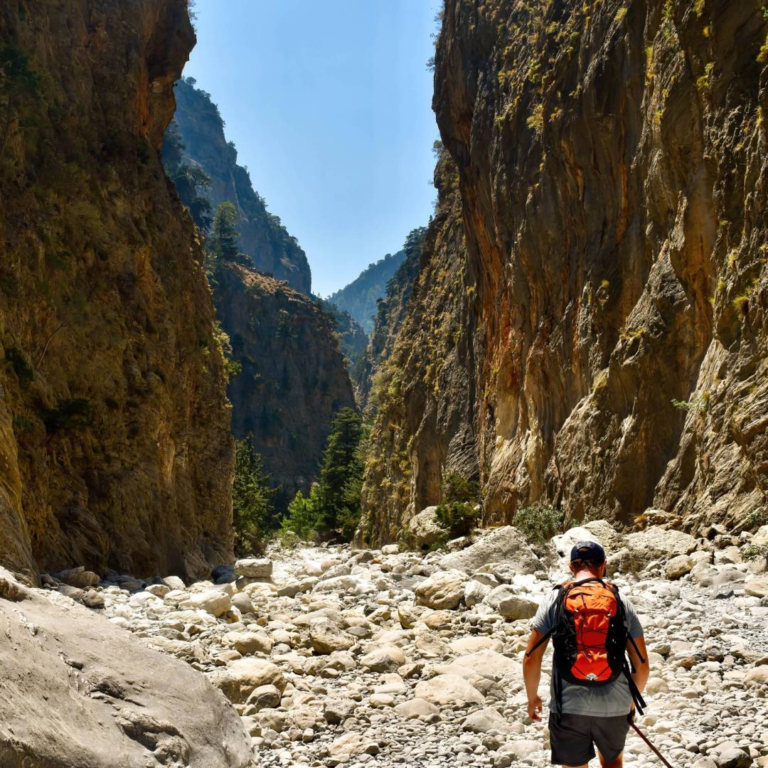Man with orange backpack hiking in mountain valleys by hot summertime in Samaria Gorge in Greece