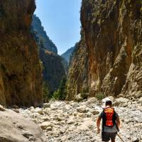 Man with orange backpack hiking in mountain valleys by hot summertime in Samaria Gorge in Greece
